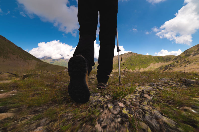 Legs of an athletic woman in black trousers and trekking boots with trekking poles walks high in the