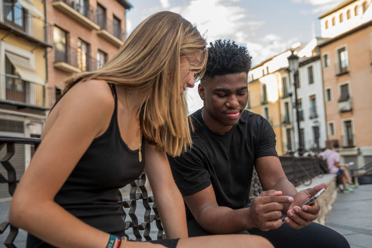 Young black boy and blonde caucasian girl sitting in a city square.