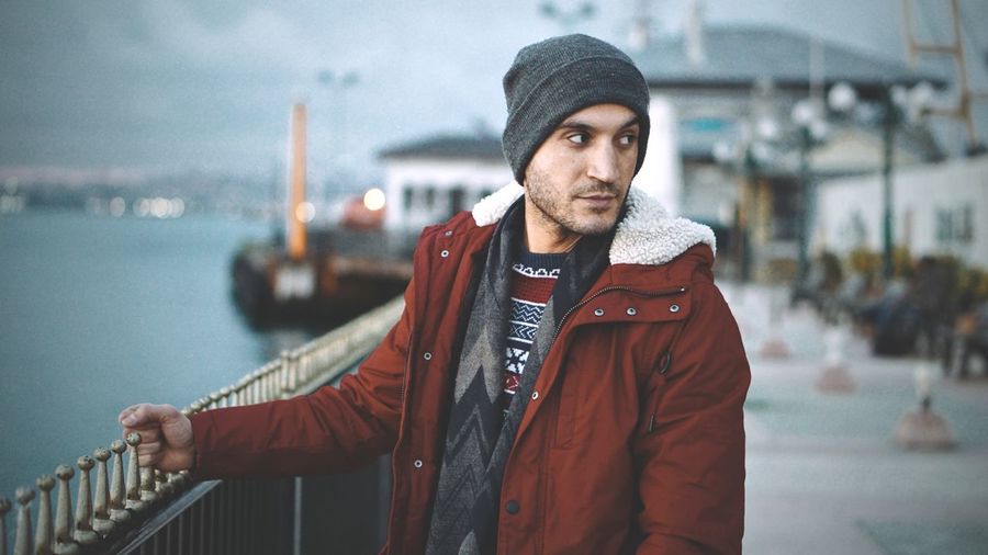 Young man in warm clothing looking away while standing by railing