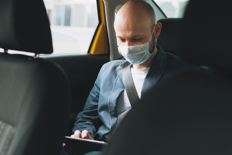 Man wearing mask using digital tablet in car