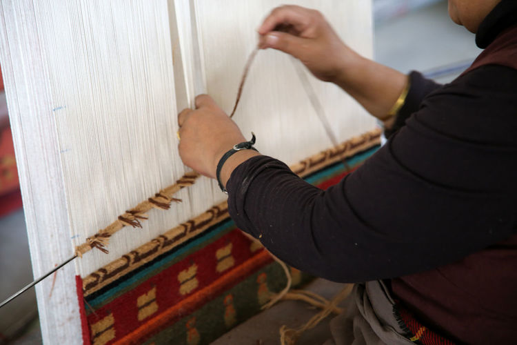 Cropped image of woman hand weaving carpet on loom