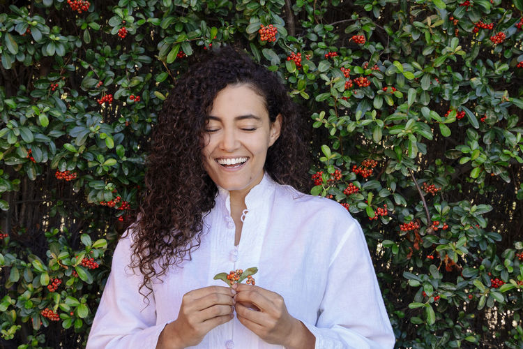 Happy young woman holding flower against plants