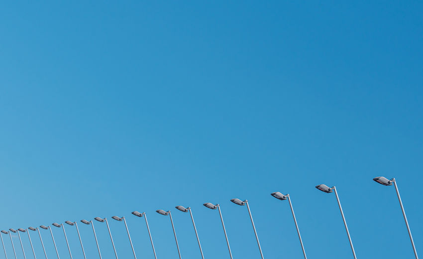 Low angle view of birds perching on cable against blue sky