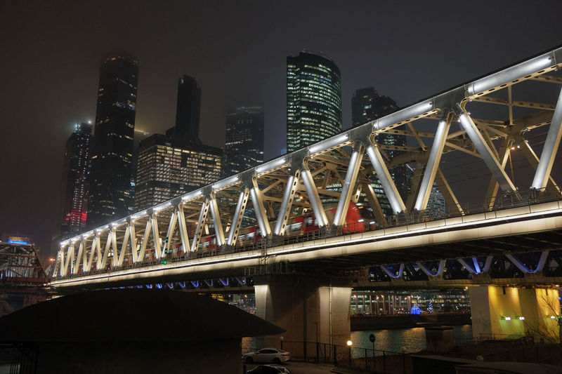 Low angle view of illuminated bridge and buildings against sky at night