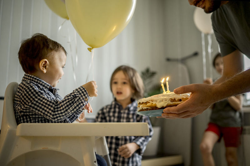 Father holding cake and celebrating son's birthday at home