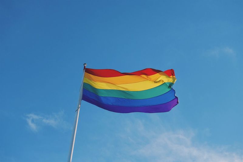 Low angle view of rainbow flag against blue sky