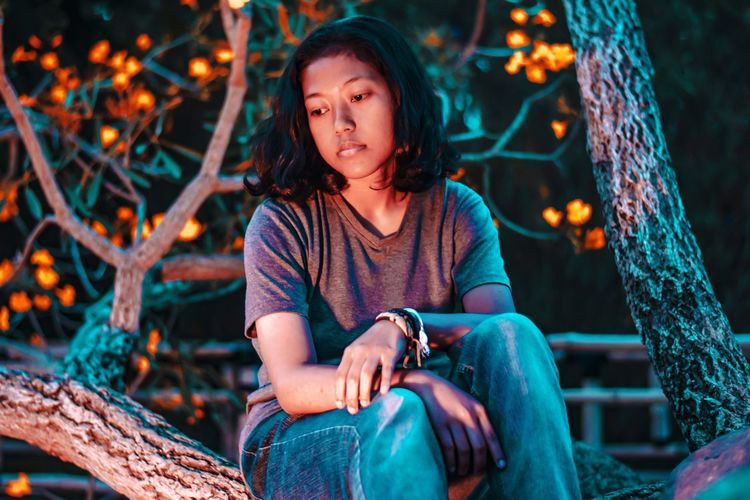 Thoughtful woman sitting against illuminated tree
