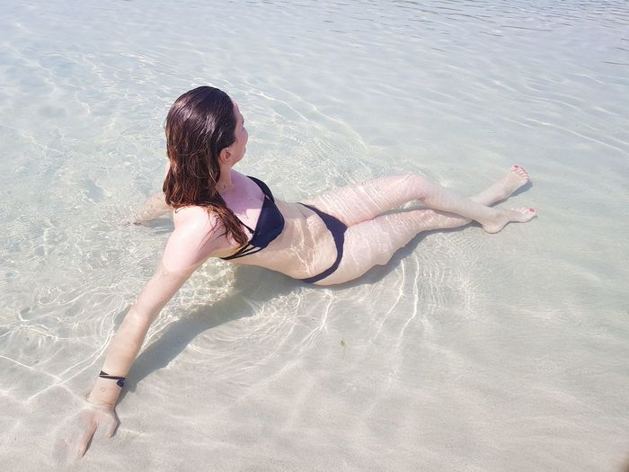 High angle view of sensuous woman wearing bikini while sitting in sea at beach