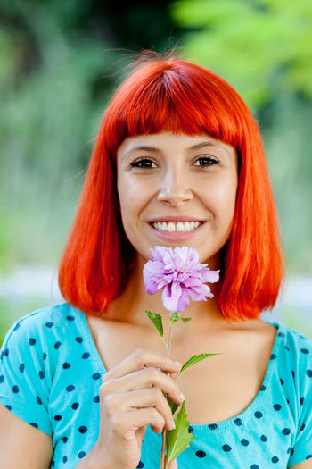 Close-up portrait of smiling woman with redhead holding flower