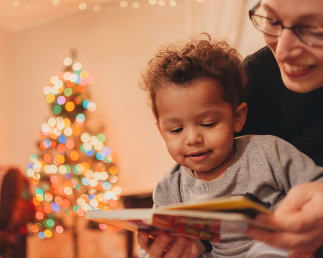 Close-up of mother with baby son reading book at home during christmas