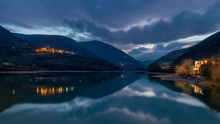 Scenic view of lake by illuminated mountains against sky