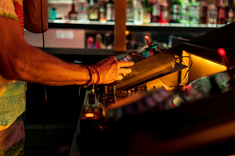 Crop unrecognizable male dj spinning and mixing music at turntable during party in illuminated nightclub