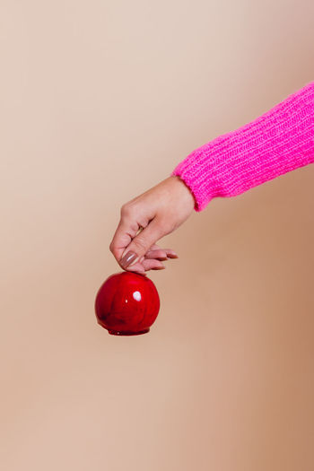 Cropped hand of woman holding tomato against pink background