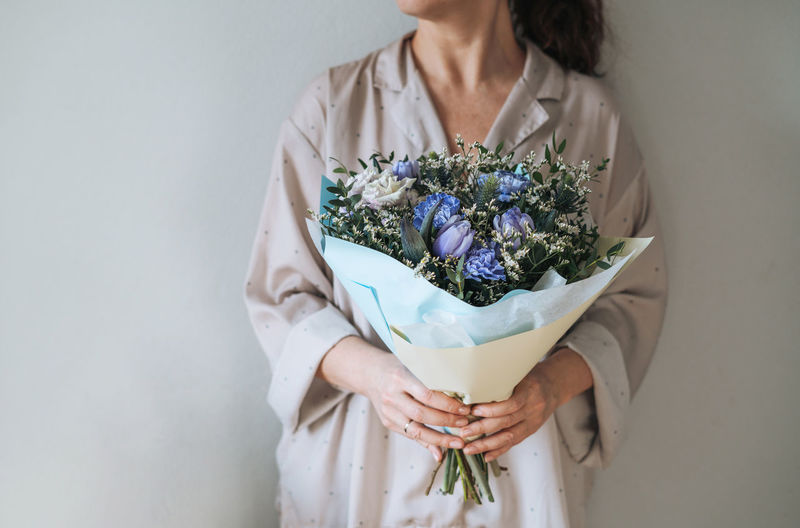 Woman in home clothes with bouqet of blue and lilac flowers in hands on the grey background