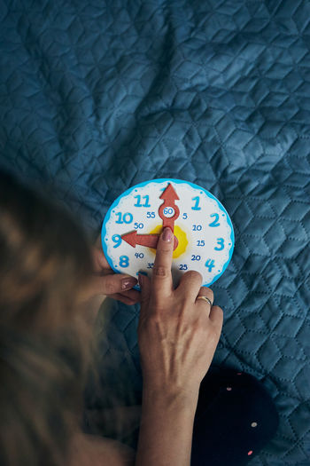 High angle view of woman hand over toy clock on bed