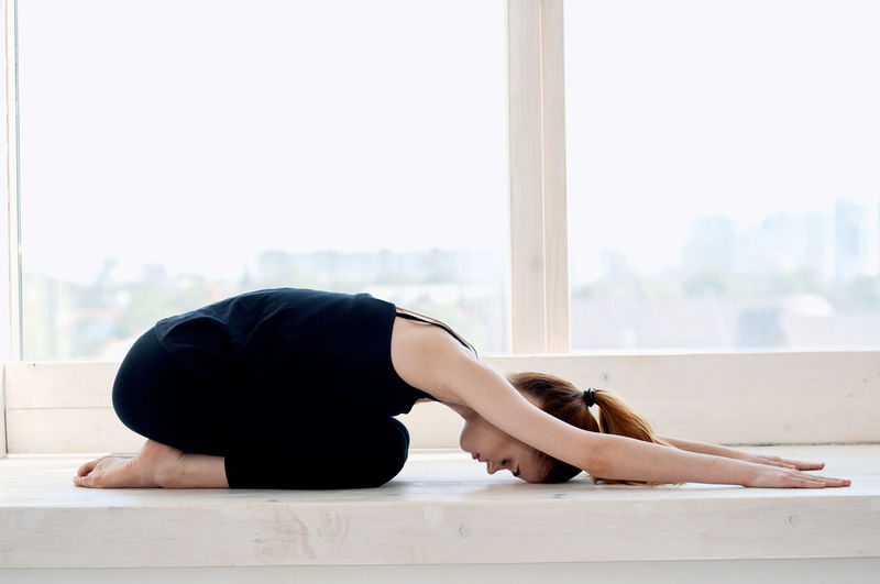 Full length of young woman relaxing on floor against window