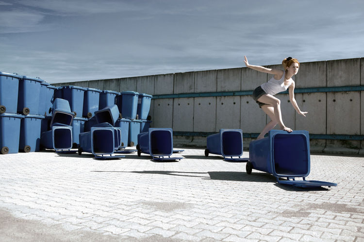 Young woman jumping on garbage bins