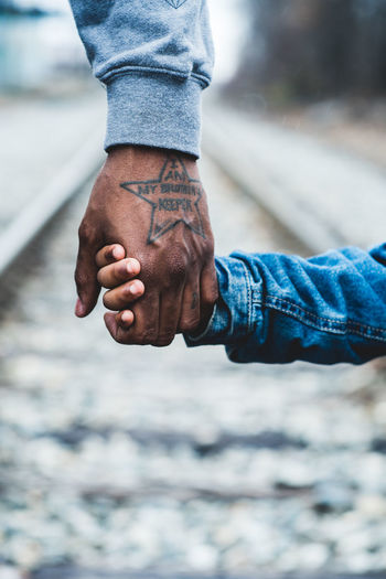 Cropped image of father and son holding hands on railroad track