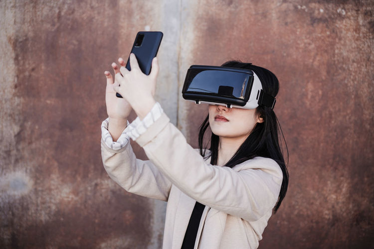 Chinese businesswoman using virtual reality headset and mobile phone in city. technology