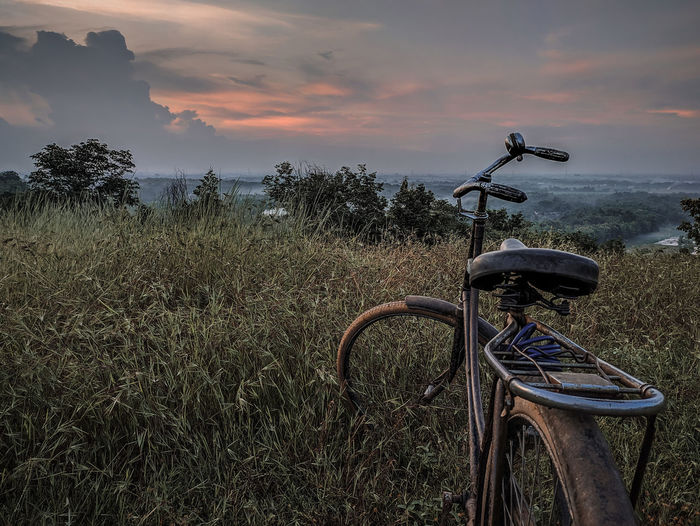 Bicycle parked on field against sky during sunset