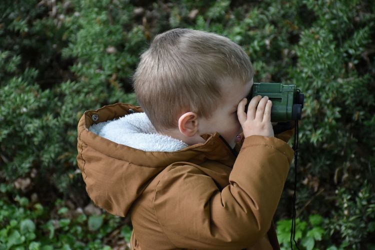 Side view of man photographing through camera against trees