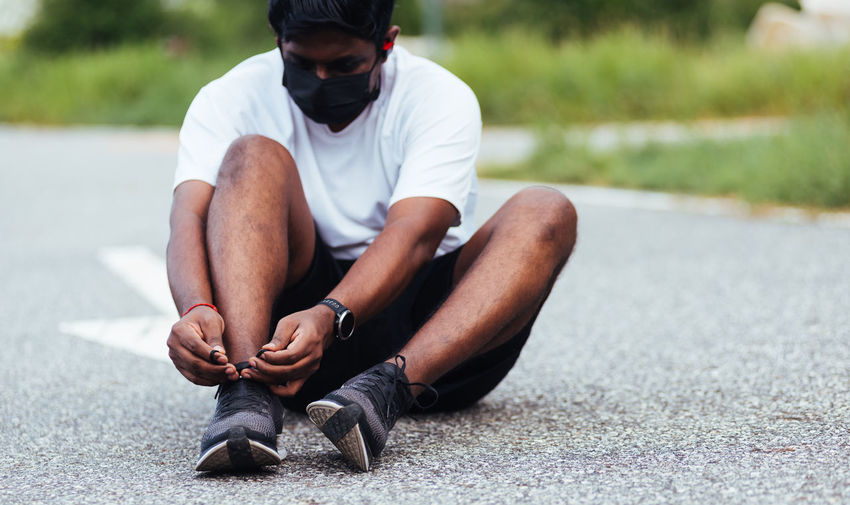 Full length of man tying shoe lace sitting on road