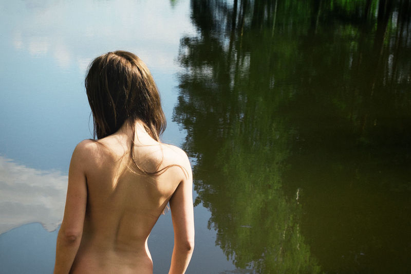 Rear view of shirtless woman standing at lake