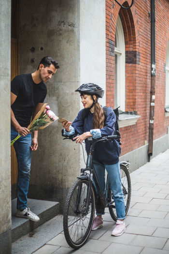 Delivery woman showing mobile phone to male customer while delivering bouquet