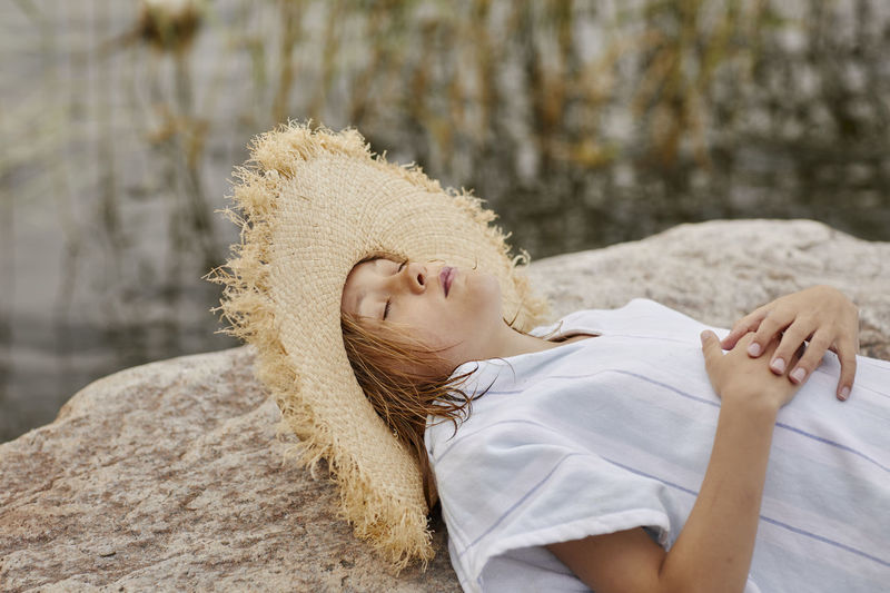 Girl wearing straw hat resting at lakeside