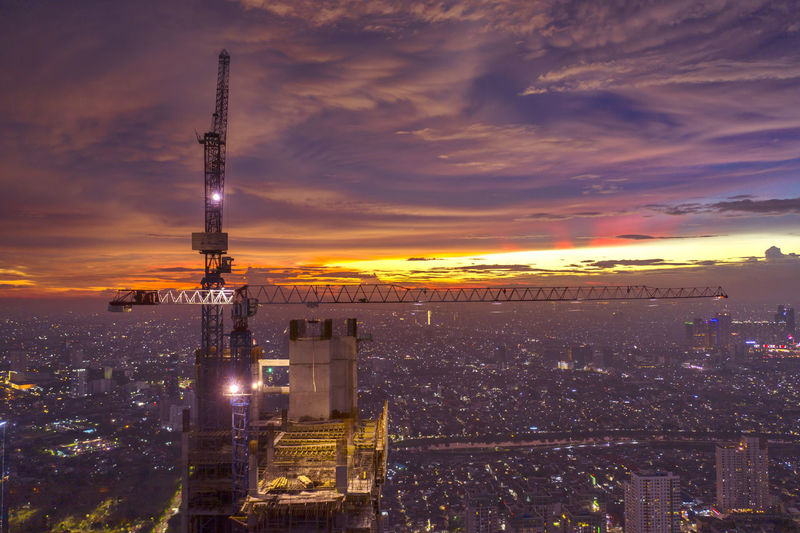 Aerial view of crane against cityscape during sunset