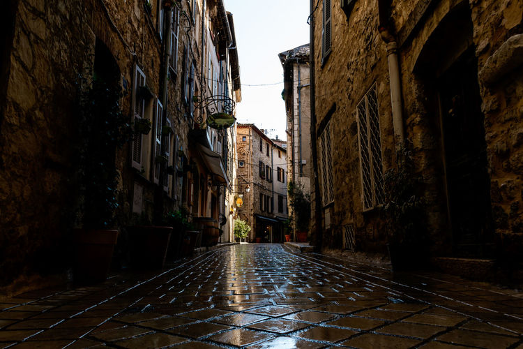 Wet footpath amidst buildings in city during rainy season