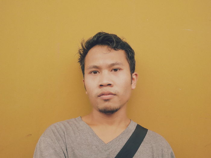 Portrait of young man standing against yellow wall