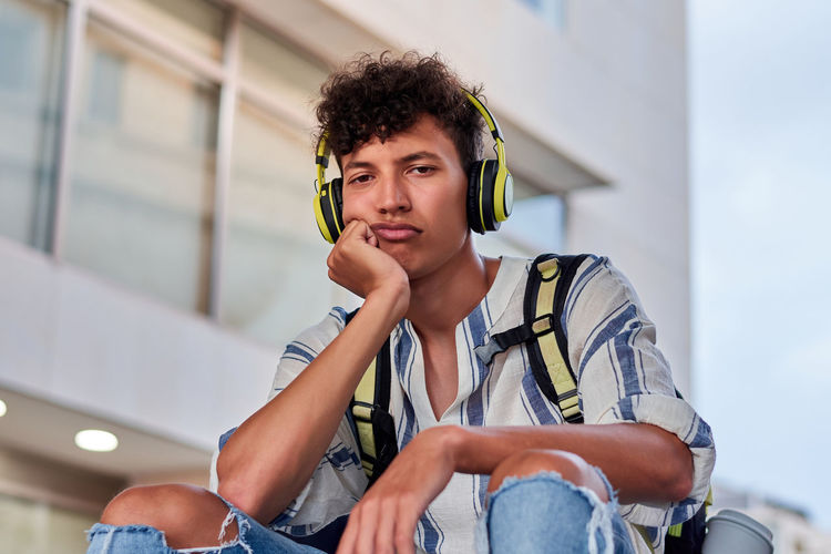 Boring young afro with headphones on sitting on the street