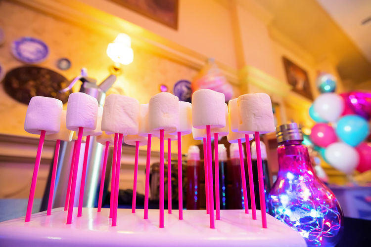 Pink marshmallows on bright pink sticks on a blurred background of the room and holiday decorations