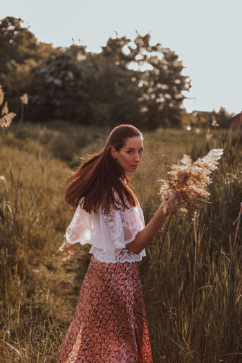 Young brunette women in a white blouse and long skirt with a bouquet of dried flowers in the field 