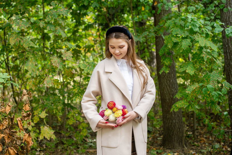 A cute girl with a red manicure with flowers in her coat pocket corrects the composition and smiles