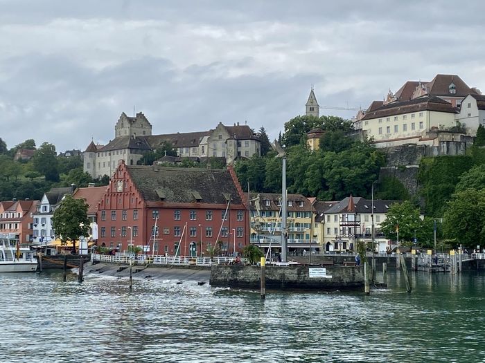 View of buildings by lake against cloudy sky