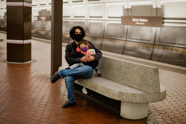 Father and daughter waiting on subway platform wearing face masks