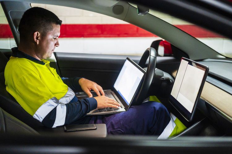 Male technician programming on laptop while sitting in electric car