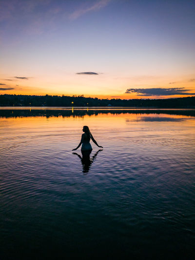 Silhouette man in swimming pool by lake against sky during sunset