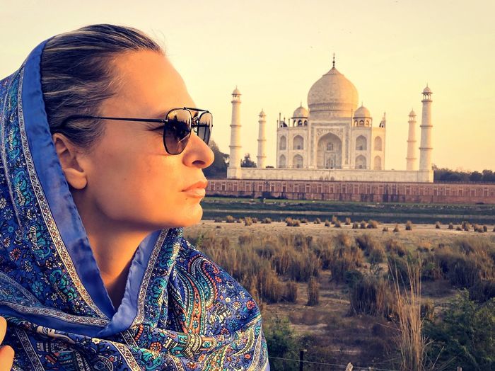 Woman wearing sunglasses with scarf standing against taj mahal