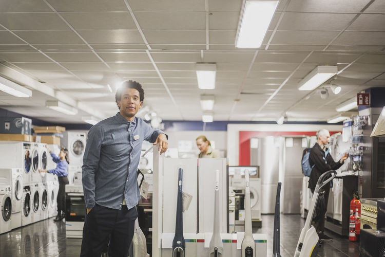 Portrait of male owner with hand in pocket standing in electronics store