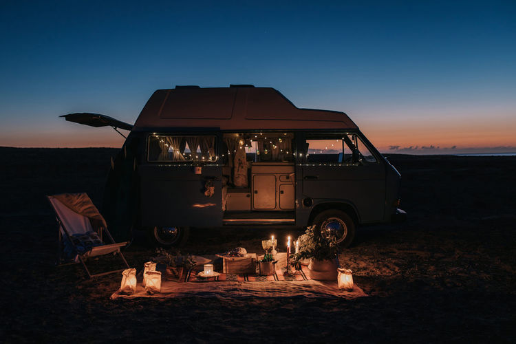 Side view of unrecognizable man making proposal for loving woman while standing on knee near illuminated van at night