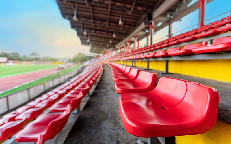 Empty red seat on grandstand for fans cheering at football stadium with evening sky