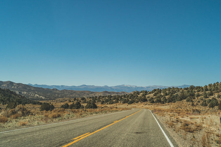 Road leading towards mountains against clear blue sky