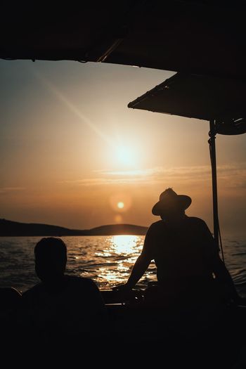 Silhouette people in ferry boat against sky during sunset
