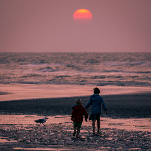 Two kids walking on the beach to the sunset.