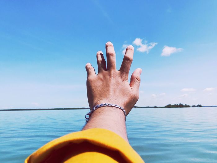 Close-up of hand wearing bracelet at sea against sky
