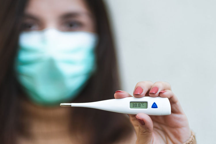 Close-up of woman wearing mask holding thermometer