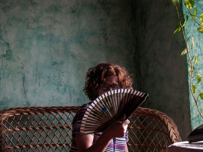 Portrait of woman covering face with hand fan at home